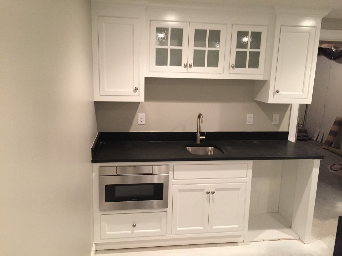 BelPort Building & Remodeling finished basement kitchenette with white cabinets and black countertop in Chatham, MA
